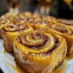 Freshly baked Banana Bread Cinnamon Rolls topped with cream cheese frosting on a wooden table.