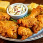 Golden-brown Louisiana fried chicken pieces arranged on a plate, garnished with parsley, with traditional Southern sides like coleslaw and cornbread in the background.