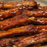 Close-up of sticky honey garlic ribs on a plate, garnished with sesame seeds and green onions.