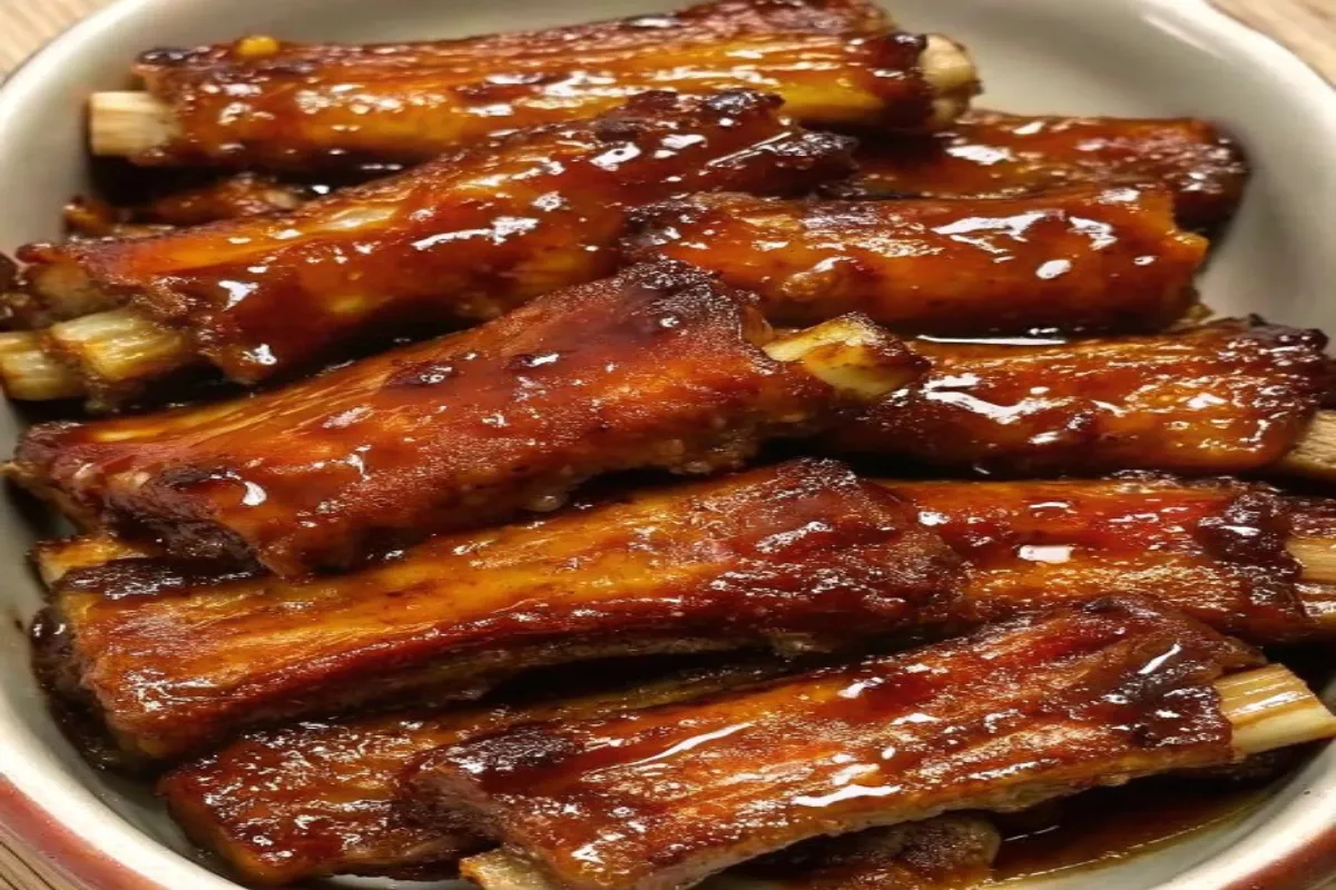 Close-up of sticky honey garlic ribs on a plate, garnished with sesame seeds and green onions.